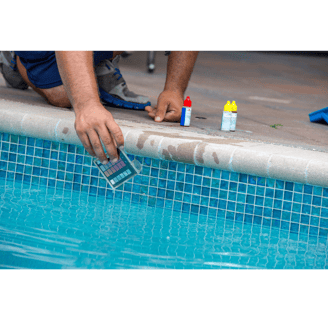 Close-up image of a pool tech kneeling on the edge of a pool performing water testing and balancing