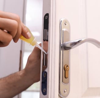 Hand applying lock lubricant to a door lock to prevent sticking and ensure smooth operation