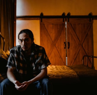 a man sitting on a bed in a bedroom contemplating relapse