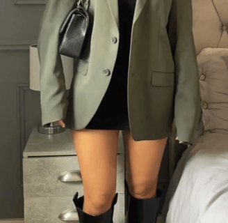 a woman in a black dress and boots is standing in front of a bed