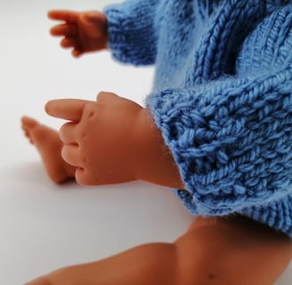 Miniland doll sitting wearing blue knitted jumper