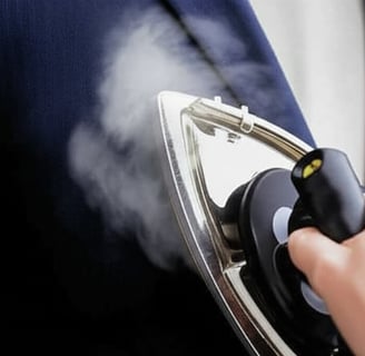 An iron steaming a dark blue suit jacket.
