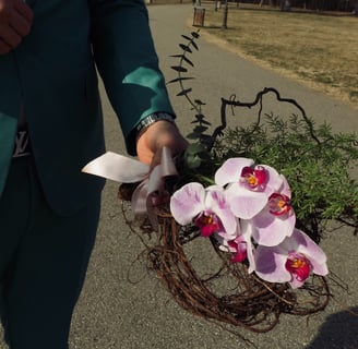 Aranjament cu orhidee, verdeață și ramuri, ținut în mână.