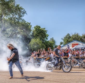 a man playing a guitar in front of a crowd with a man burning out on his motorcycle.