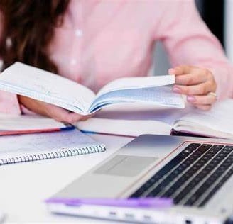 a woman is sitting at a desk with a laptop and a notebook