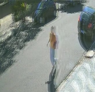 a woman walking down a street with a car parked in front of her