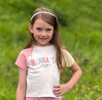 a young girl standing in a field with a baseball bat