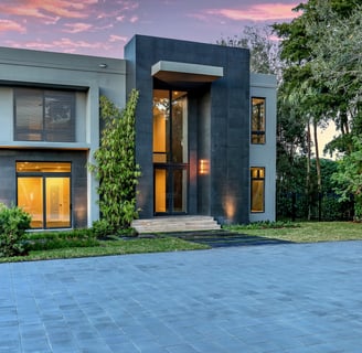 a luxury home lit up at night with a large driveway and a vibrantly colored sky