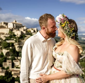 Fine art couple session — bride with flower crown gazes at partner with Provençal village backdrop