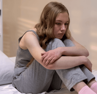 Mujer jovencita sentada en su cama pensando acerca de los sentimientos de ansiedad que experimenta
