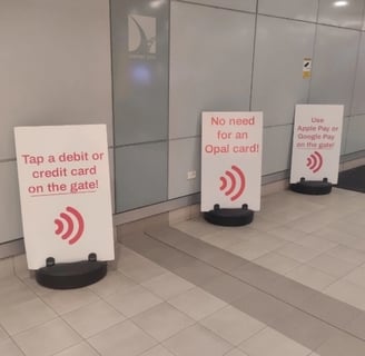 Three white signs stand on a tiled floor in what appears to be the Sydney Airport.
