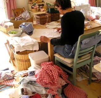 a woman sitting at a table with a lot of clothes on it