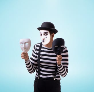 A mime with white face makeup and black fake teardrop holding a white mask and a black mask in each
