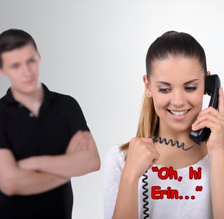 A man with a jealous look standing behind a woman talking on a phone