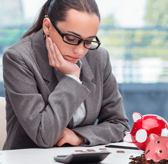 A sad woman sitting at a desk looking at her broken piggy bank and coins