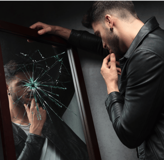 a man in a leather jacket is looking at a broken mirror