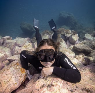 A freediver in a wetsuit is posing for an underwater photoshoot. Photo taken by Sébastien Saintignan
