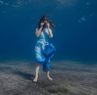 a model in a blue dress is standing in the water during an underwater photoshoot.