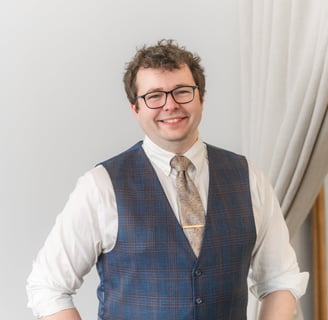Picture of Rocco Catrone smiling at camera with glasses, a gold tie, and vest.