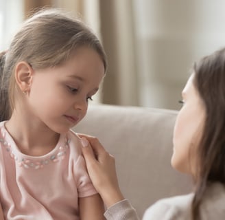 a woman in a pink shirt is resting her hand on a little girl's shoulder