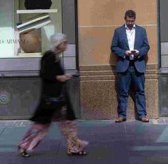 Man standing motionless against wall while blurred woman passes in front of him