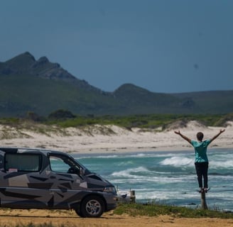 Man standing on short pole near car on beach