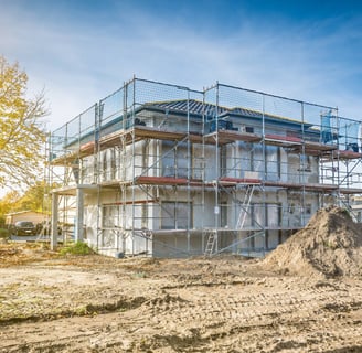 Eingerüstetes Gebäude während der Sanierungsarbeiten mit Baumaterial und Erdarbeiten im Vordergrund