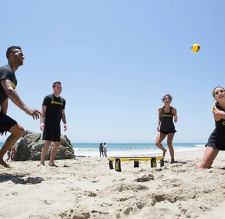 deux équipe de deux personnes s'affrontent au spikeball sur la plage