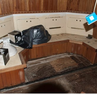 settee with some boat parts and a garbage bag on top in an unfinished interior made of wood