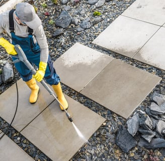 A man in blue clothes pressure washing some large stones