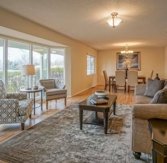 Living room with sofa, coffee table, and two chairs and dining room towards the back