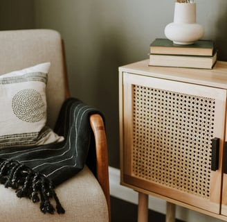 Un fauteil avec un plaid, à côté un vase et des livres posés sur un meuble en bois