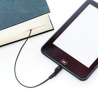 An iPad is connected to a hardbound book with USB cable from the iPad to the hardbound book. 