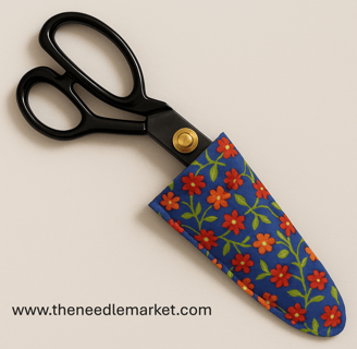 A pair of black tailor’s shears with gold pivot detail partially enclosed in a handmade fabric case.