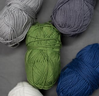 Colorful skeins of yarn in gray, green, blue, and white tones arranged on a neutral fabric backgroun