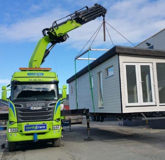 House being lifted onto a truck by a knuckle boom lorry mounted crane.