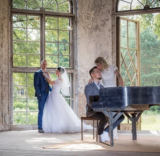 Ein Brautpaar küsst sich an einem Klavier in einer lichtdurchfluteten Umgebung.