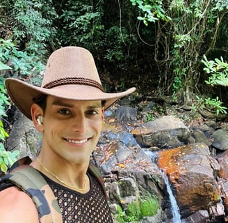 Rick Rockefeller-Silvia with a safari hat, smiling in front of a waterfall in Phuket, Thailand