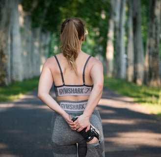 Woman stretching her leg on a sunlit tree-lined path, symbolizing active living, mobility.