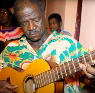 Sr. João tocando violão, símbolo da música e tradição oral de São Tomé