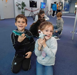 2 enfants à genoux souriants qui tiennent des figurines de requins dans les mains