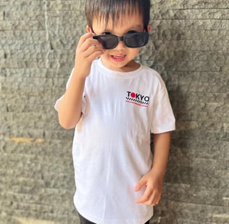 Anak laki-laki memakai kaos putih Tokyo High Performance Sports dari RŪMI Kidswear, gaya streetwear keren.