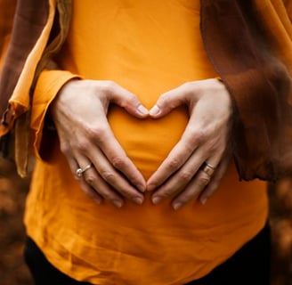 mum to be making a heart shape on her tummy wearing a orange top