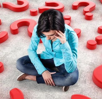 A thinking woman sitting on a floor with multiple red question marks around