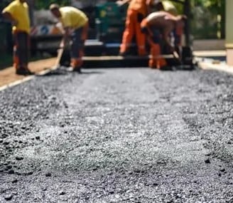 Men spreading ashpalt ahead od the asphalt paver. 