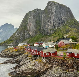 Ikoniske røde rorbuer ved sjøen i Hamnøy, Lofoten, omgitt av majestetiske fjell og arktisk kystlands