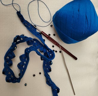 ouvrage bleu au crochet fin avec des perles noir et deux crochets le tout posé sur un fond crème 