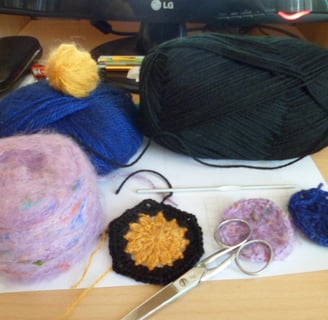 Pelotes de laines posées sur une feuille blanche qui est posé sur une table un crochet au milieu