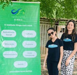Uma criança e uma mulher em pé ao lado de um banner do Instituto Xingu MT