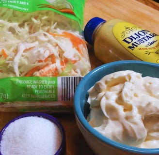 Coleslaw ingredients arranged on a wooden cutting board, including cabbage, carrots, and seasoning items